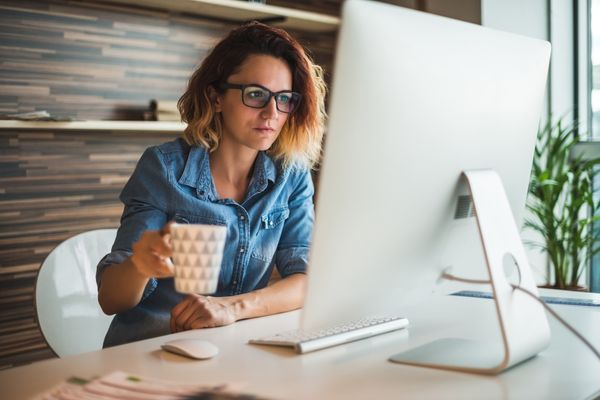 mulher sentada em frente ao computador, com uma xícara na mão, planejando com o tarô.