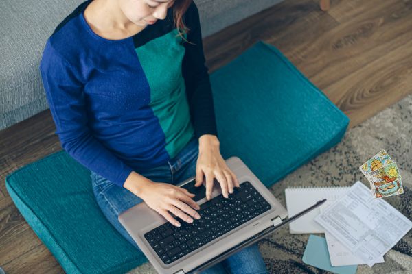 Mulher oriental sentada no chão com um laptop no colo. Ao lado dela, cartas de tarô para organizar o seu dia a dia.