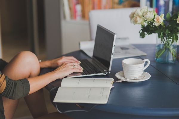 mão feminina digitando no laptop sobre a mesa, com uma xícara de café ao lado. Organização sem estresse.